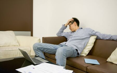 Stressed Asian businessman using a smartphone in living room at nightの写真素材