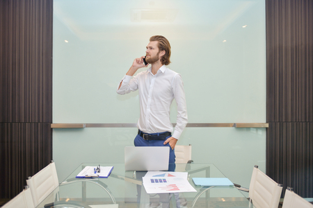 Blonde business man talking on the phone with blank glass boardの写真素材