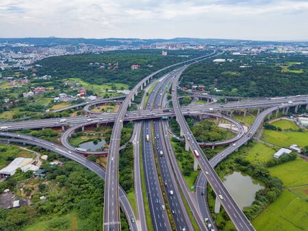Aerial view of cars driving on highway junctions. Bridge roads with green garden and trees in...
