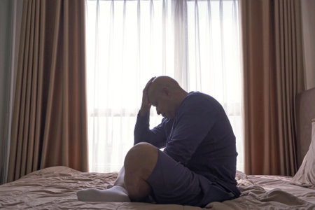 Depressed lonely old elderly black man. African American people sitting on bed with windows in bedroom at home in early morning. Quarantine lifestyle. Unhappy life.の写真素材