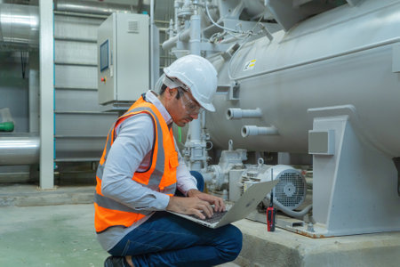 An engineer man or worker, people using a laptop computer, working in industry factory. Chiller tower or cooling tower in building. System work machine. Condenser Water Supply pipe lines. Ventilation.の写真素材