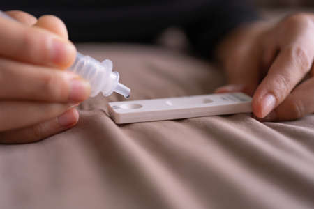 Hand holds a test cartridge at home. COVID-19 Ag rapid self test kits on bed at home in quarantine....