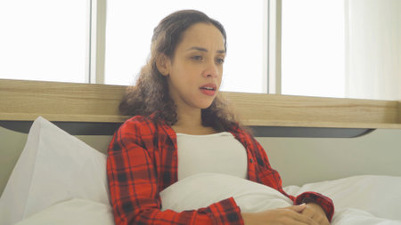 Depressed lonely sad emotional business latin woman is fired from job, crying. Sitting on bed in bedroom at home in early morning. Quarantine lifestyle. Unhappy life.の写真素材