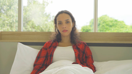 Depressed lonely sad emotional business latin woman is fired from job. Sitting on bed in bedroom at home in early morning. Quarantine lifestyle. Unhappy life.の写真素材