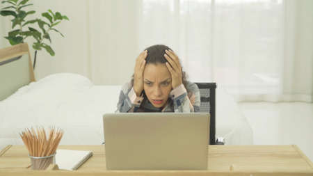 Depressed lonely sad emotional business latin woman is fired from job in front of computer laptop notebook with a bed in bedroom at home in early morning. Quarantine lifestyle. Unhappy life.の写真素材