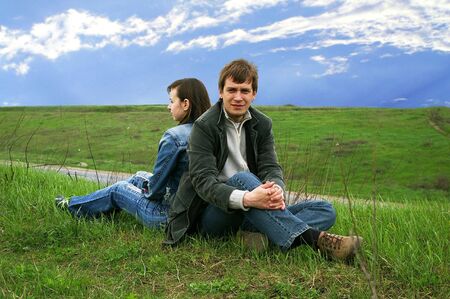 Guy and girl sits on a grass on a background of the skyの写真素材