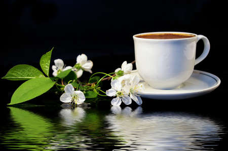 Flowers of a cherry and white cup of black coffee on a black background