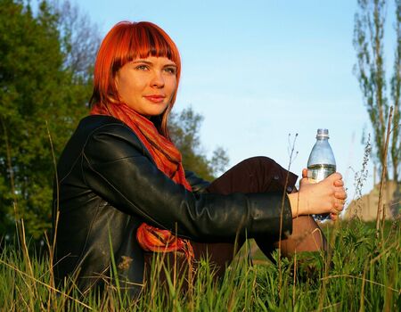 The beautiful young girl drinks water on a background of the skyの写真素材