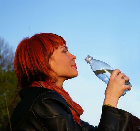 The beautiful young girl drinks water on a background of the skyの写真素材