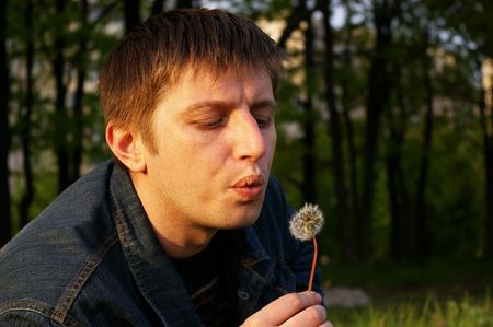 Man blowing dandelion with blue sky and treesの写真素材