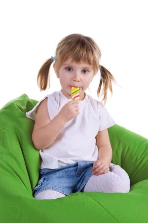 Little girl with a bright lollipop sit on green armchairの写真素材