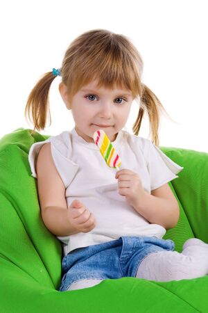 Little girl with a bright lollipop sit on green armchairの写真素材
