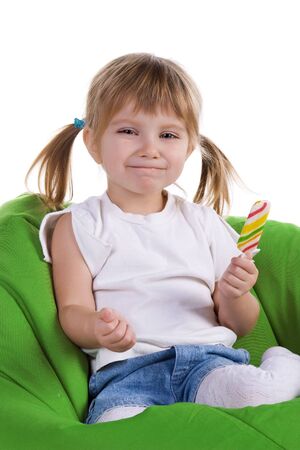 Little girl with a bright lollipop sit on green armchairの写真素材