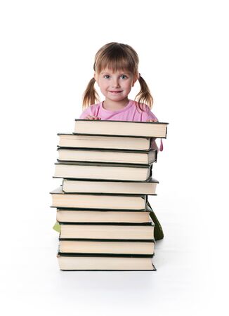 Cute little girl sit near a stack of big books on white backgroundの写真素材