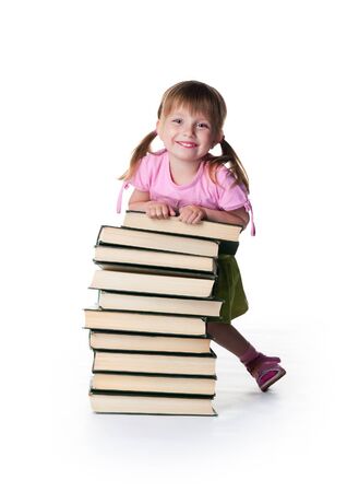 Cute little girl sit near a stack of big books on white backgroundの写真素材