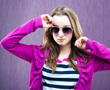 portrait of a beautiful little fashion model in sunglasses on purpleの写真素材