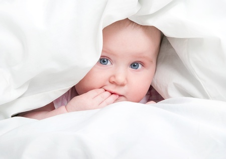 cute baby under a blanket in bedの写真素材