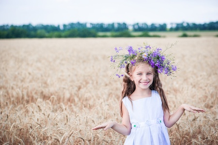beautiful smiling little girl with a wreath on his head in a field of wheatの写真素材