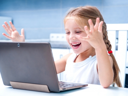 glad little girl with her computer at home at the tableの写真素材