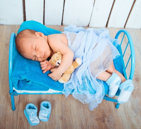 Cute newborn baby sleeps in a small bed with teddy bearの写真素材