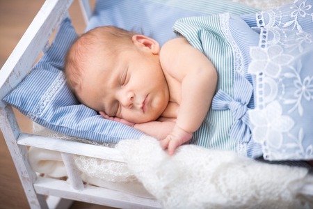 Sweet newborn baby boy sleeps in a small bedの写真素材