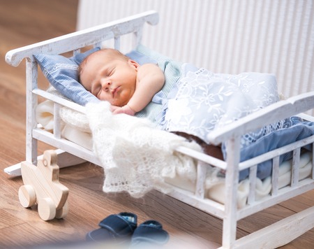 newborn boy sleeps in a small bed  nearby is a toy boatの写真素材