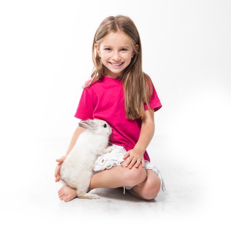 smiling little girl in a pink T-shirt with her small white rabbitの写真素材
