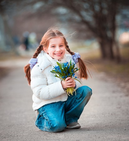 happy little girl smiling and holding a bouquet of snowdropsの写真素材