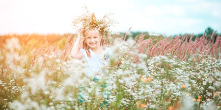 happy little girl with a wreath on her head on the field with chamomilesの写真素材