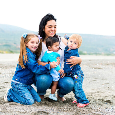 beautiful young mother playing with her kids on the beach on a sunny summer dayの写真素材