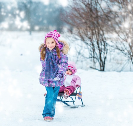 little girl sledding his sister in the winter parkの写真素材