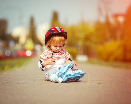 two year old pretty girl in roller skates and a helmet sitting on the street