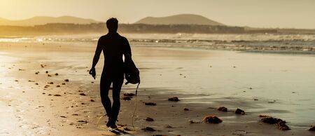 Surfer on the ocean beach at sunset on  Canary Islands. Lanzarote, Spain.