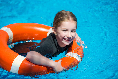 happy little girl swims in a wetsuit with a lifeline in the pool