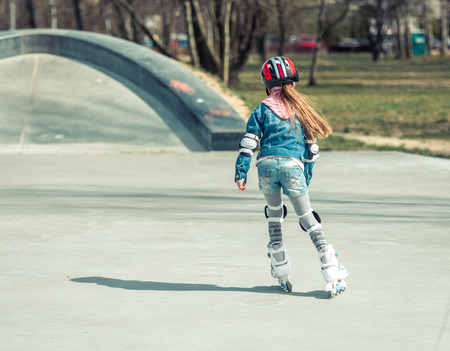 Little pretty girl on roller skates in helmet at a park. back viewの写真素材