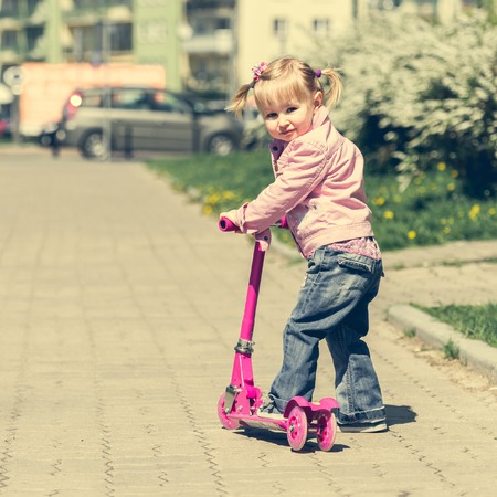 Two years old girl riding her scooter on the streetの写真素材