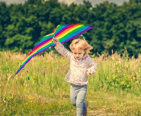 little cute girl flying a kite in a meadow on a sunny day. close-upの写真素材