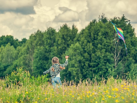 little cute girl flying a kite in a meadow on a sunny day. back viewの写真素材