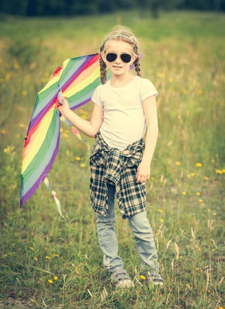 little cute girl posing with a kite in a meadow on a sunny dayの写真素材