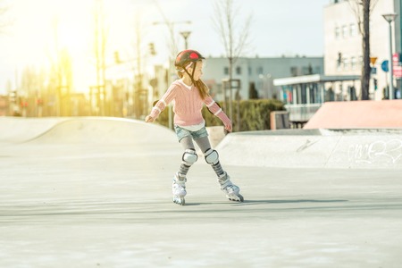 Little pretty girl on roller skates in helmet at a park