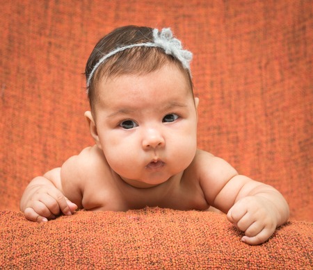 two-month-old girl with decoration on a head lies on a orange backgroundの写真素材