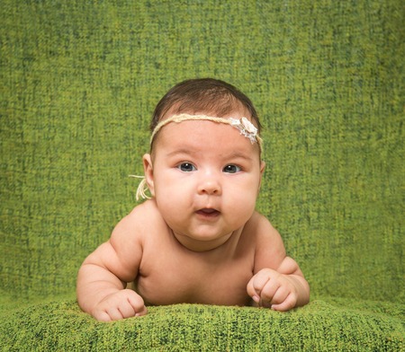 two-month-old girl with decoration on a head lies on a green backgroundの写真素材