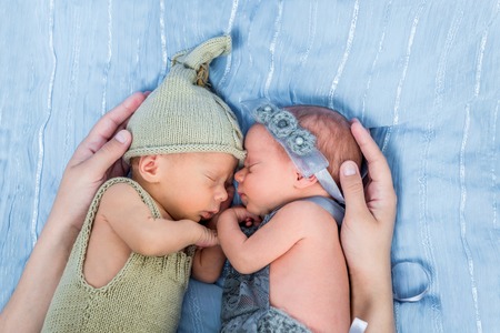 mothers arms wrapped around newborn twins  sleeping on a blue blanketの写真素材