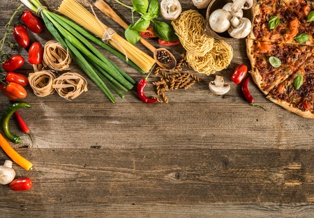 Italian food background with pizza, raw pasta and vegetables on wooden tableの写真素材