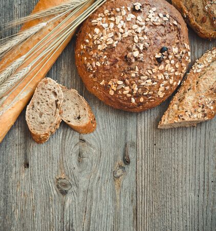 Different types of bread on a wooden table with ears of wheatの写真素材