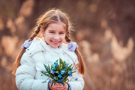 little girl smiling and holding a bouquet of blue  flowersの写真素材