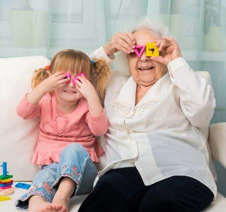 grandmother with granddaughter playing toys sitting on sofaの写真素材
