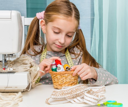 little seamstress sitting at the table with threads in basket and sewing machineの写真素材