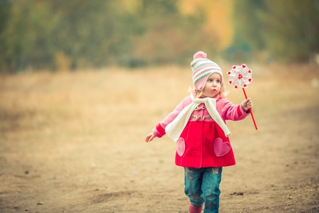little girl playing pinwheel toy walking on autumn landscapeの写真素材