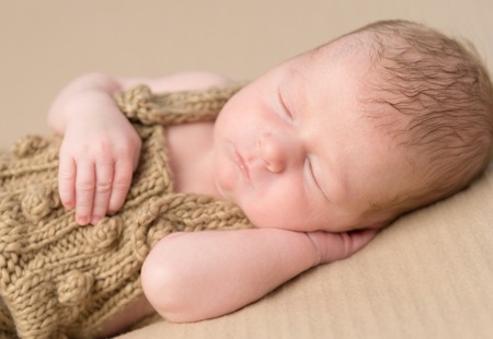 beautiful newborn baby in knitted overalls sleeping on blanket with hand under his headの写真素材